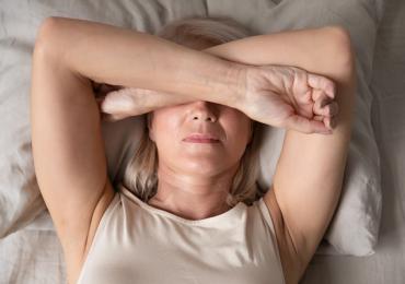 Older woman lying down on bed covering her eyes