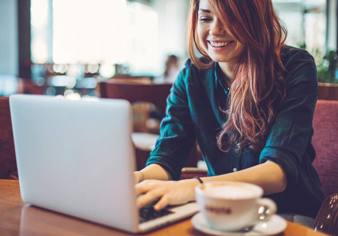 Person sitting on burgundy couch with a coffee on their laptop in coffee shop