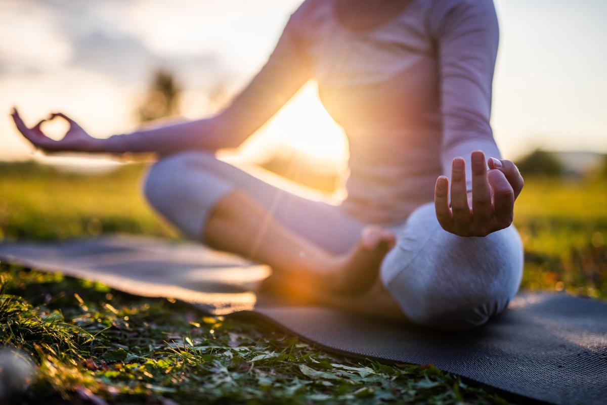 Person on mat outside in seated yoga position with their legs crossed