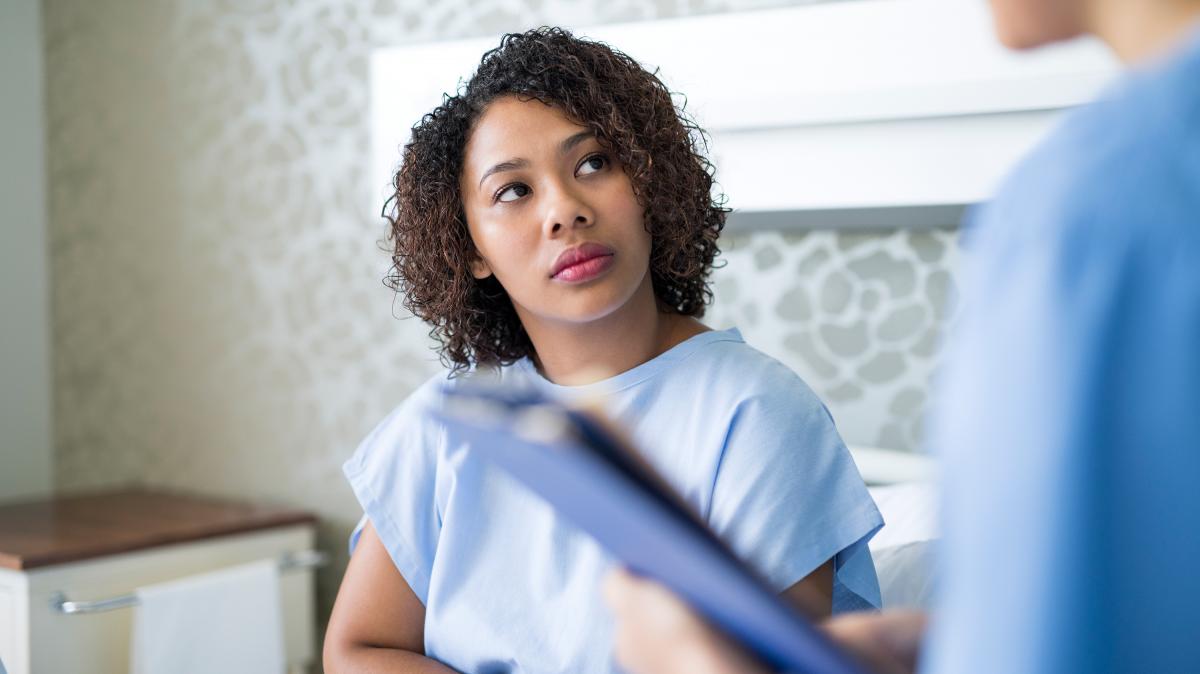 Female patient dressed in hospital gown listening to doctor