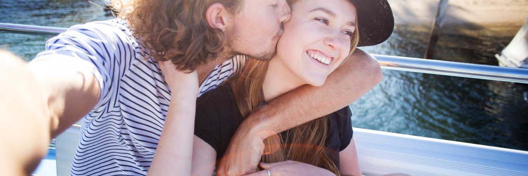 Young man kissing smiling woman on the cheek whilst taking a photo
