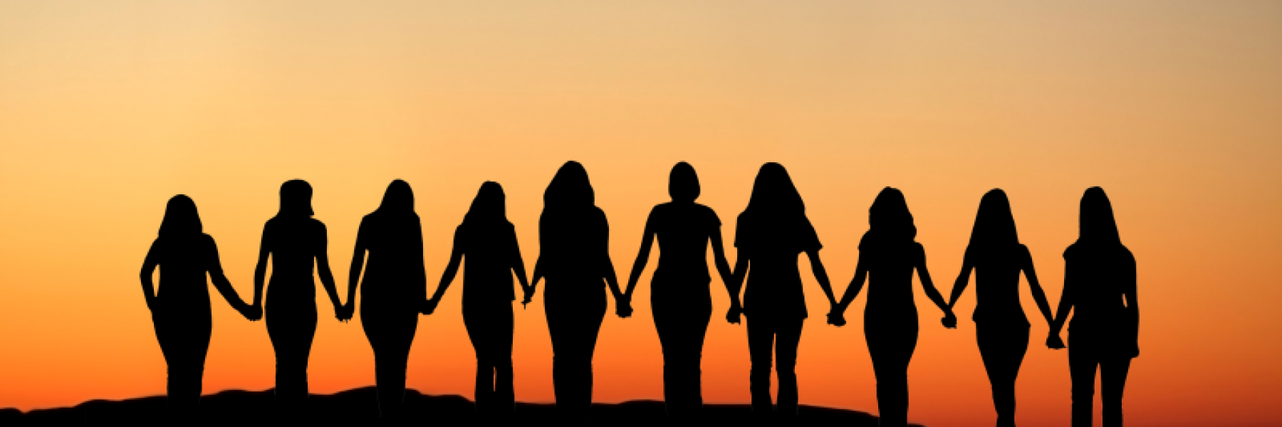 Women holding hands facing the sunset
