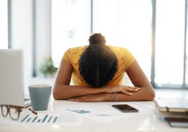 Woman exhausted, sitting at a desk, head down on her arms