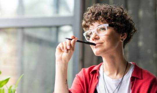 Woman looking out window with pen to her mouth